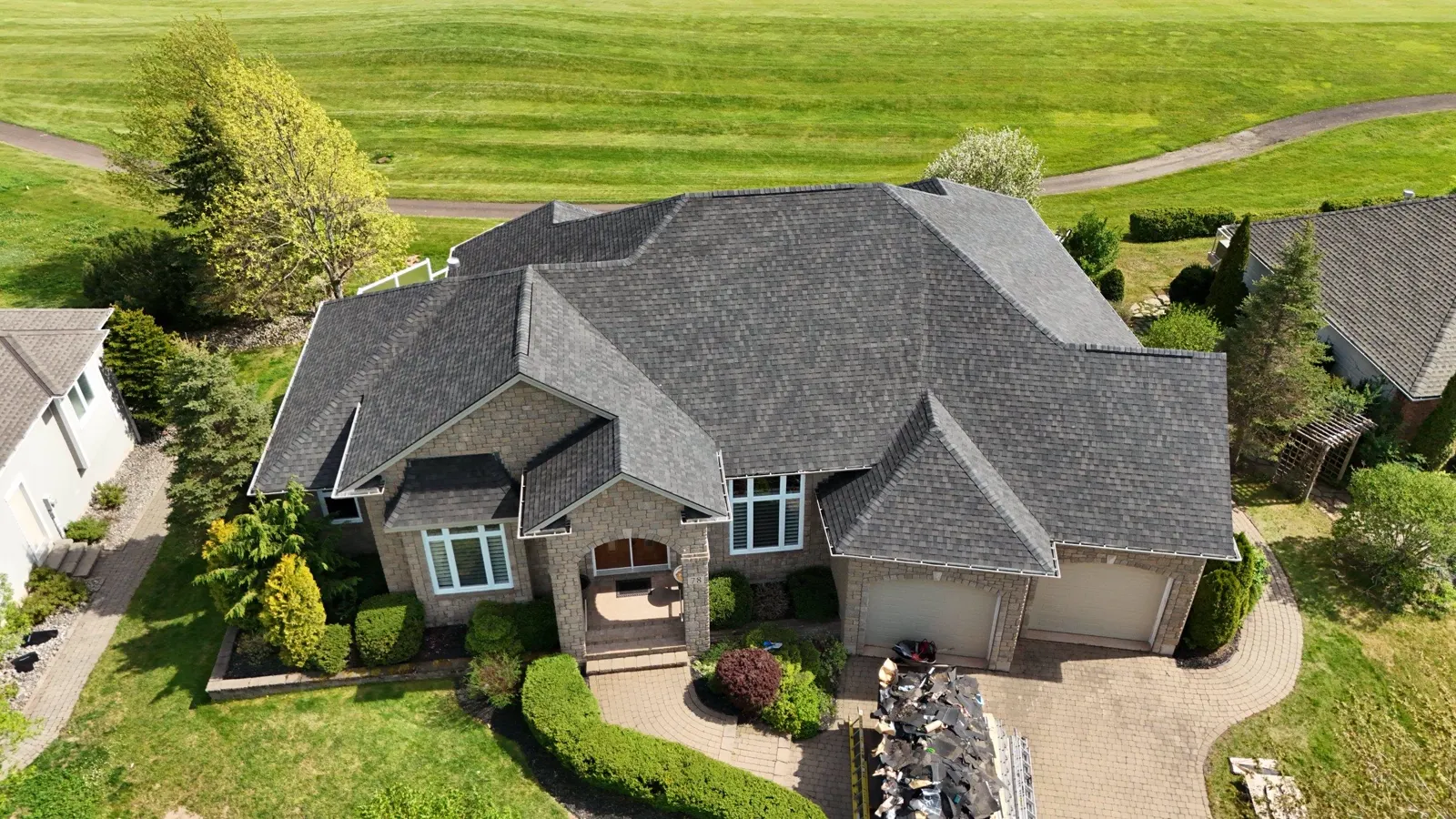 Finished architectural shingle roof on a large Moncton estate home beside a golf course pond, drone photo
