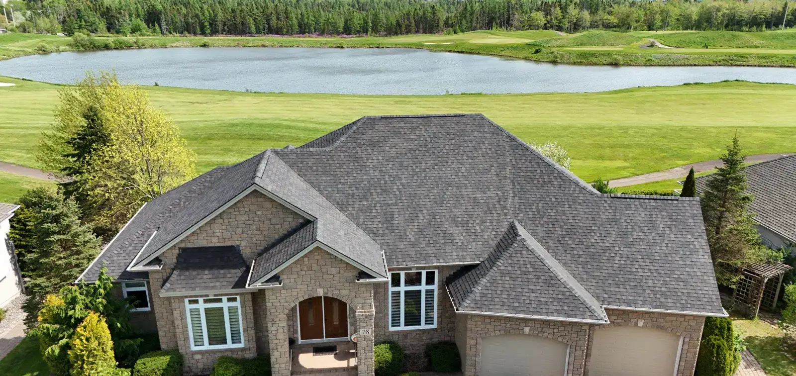 Finished roof replacement on a stone estate home in Moncton, overlooking a golf course pond, photographed by our drone