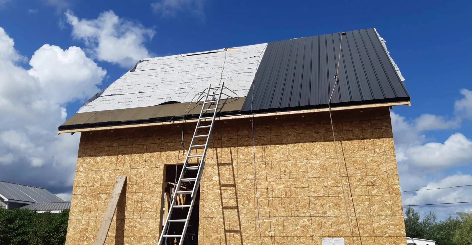 Metal roof install in progress with underlayment on one slope and finished dark steel panels on the other