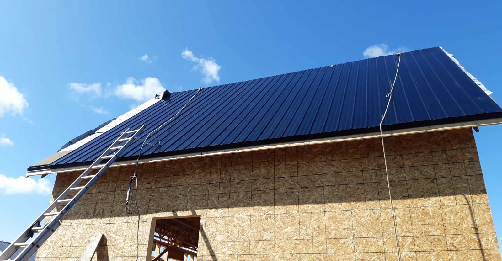 Finished dark blue standing seam metal roof on a new build in Cocagne, New Brunswick, against a clear sky